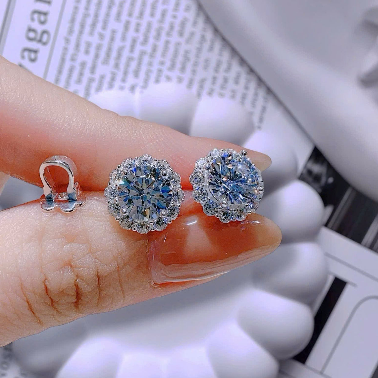 Silver earrings with gemstones held between fingers on a newspaper background