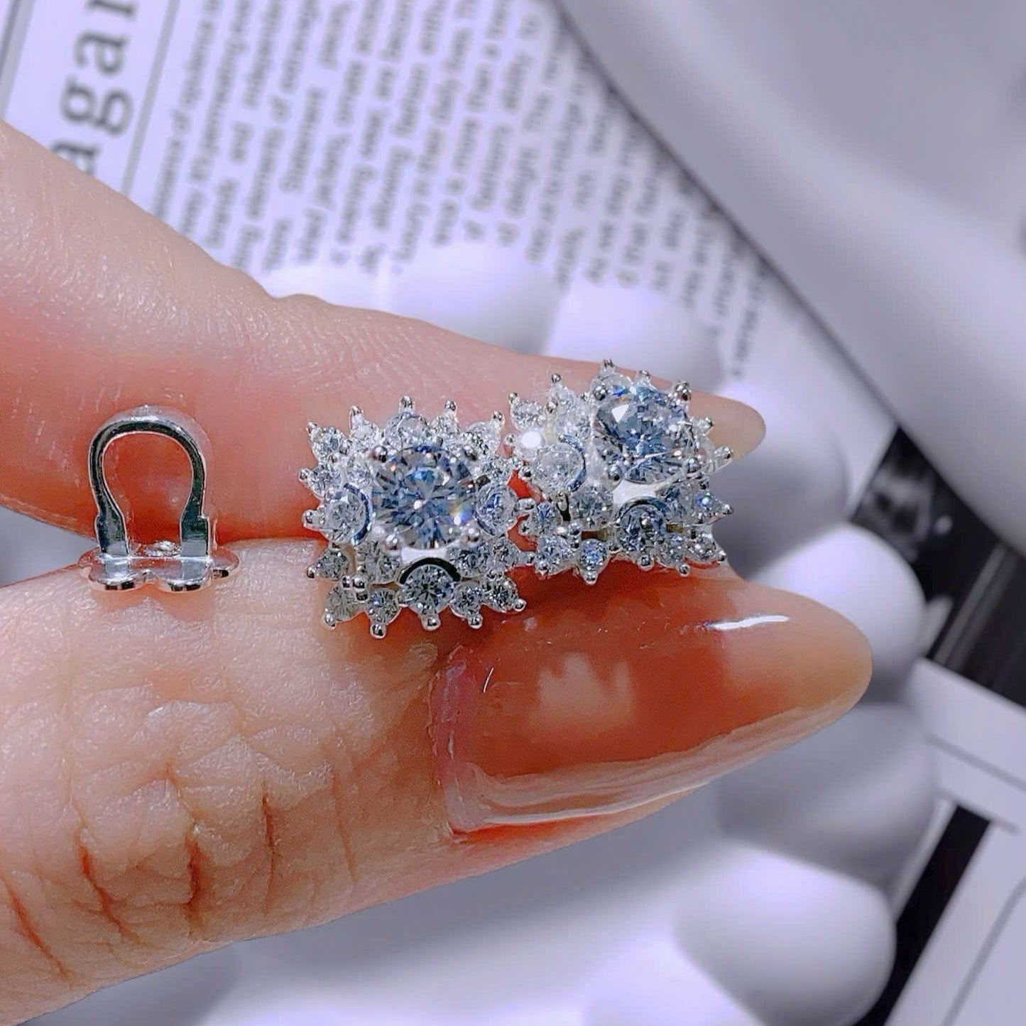 Silver earrings with gemstones held between fingers on a newspaper background