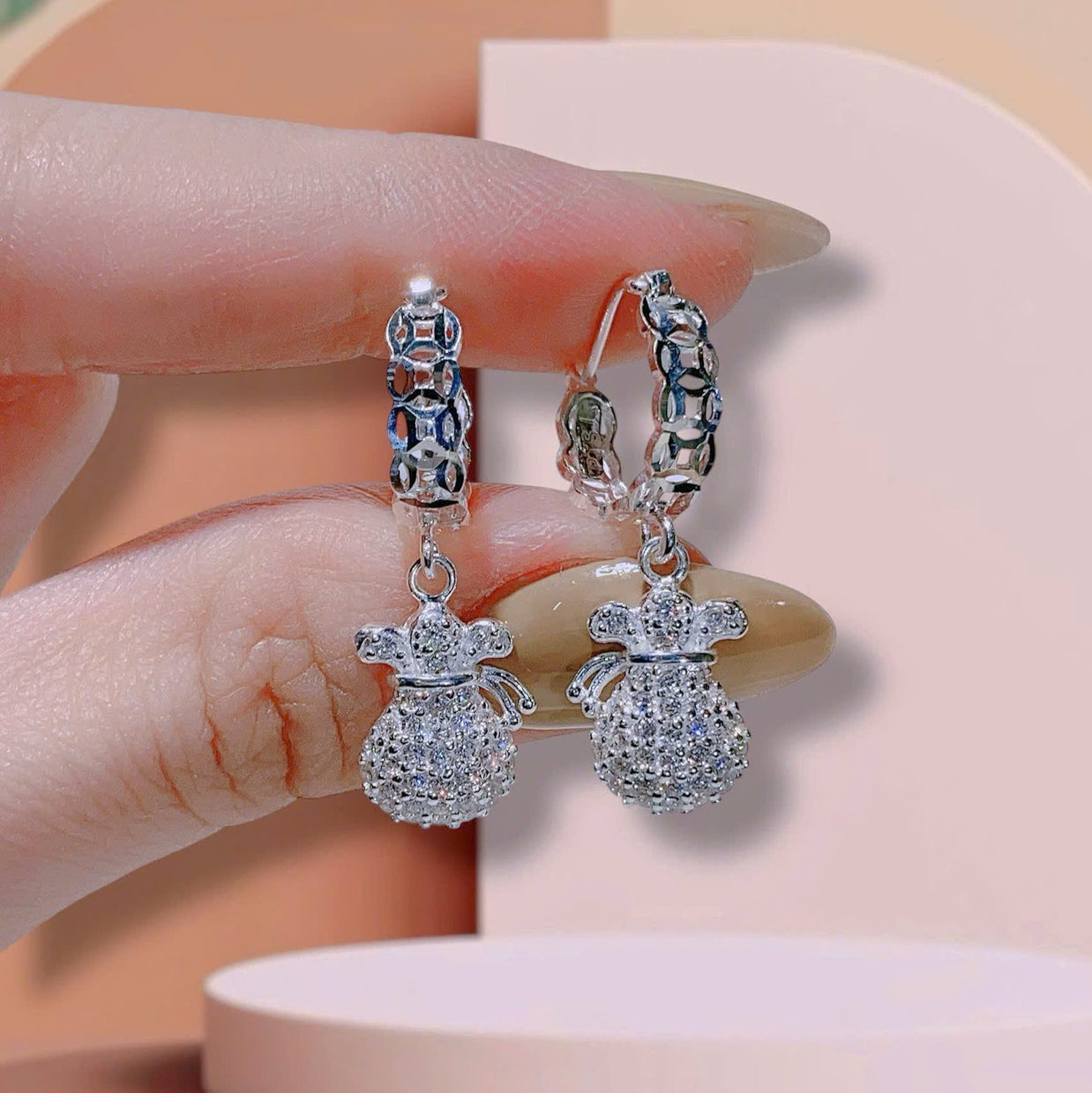 Silver earrings with gemstones held by a hand against a neutral background
