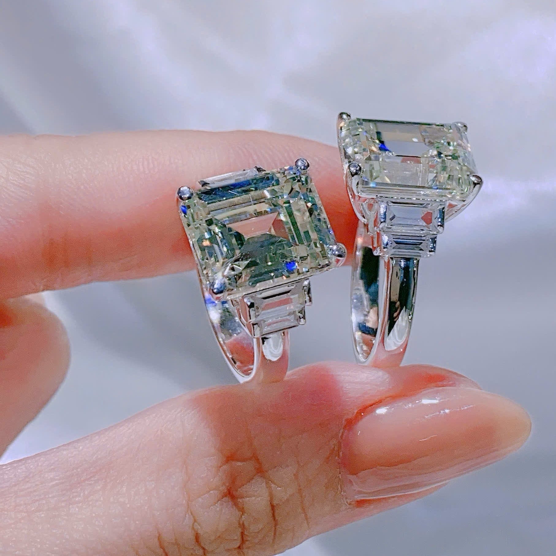 Silver earrings with green gemstones held by a hand against a white background