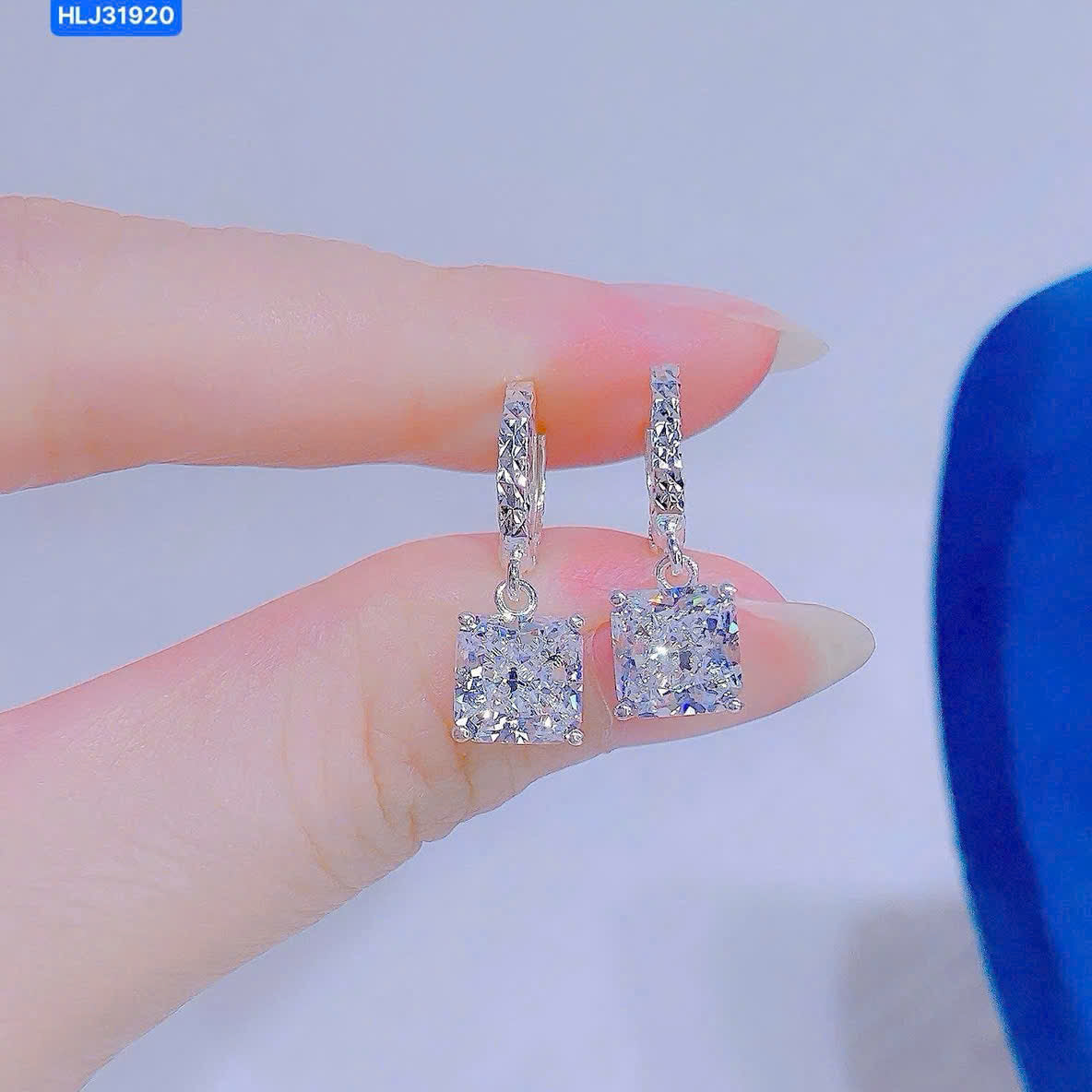 Silver earrings with square gemstones held between fingers against a light background