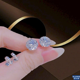 Silver flower-shaped earrings held by a hand with a dark background