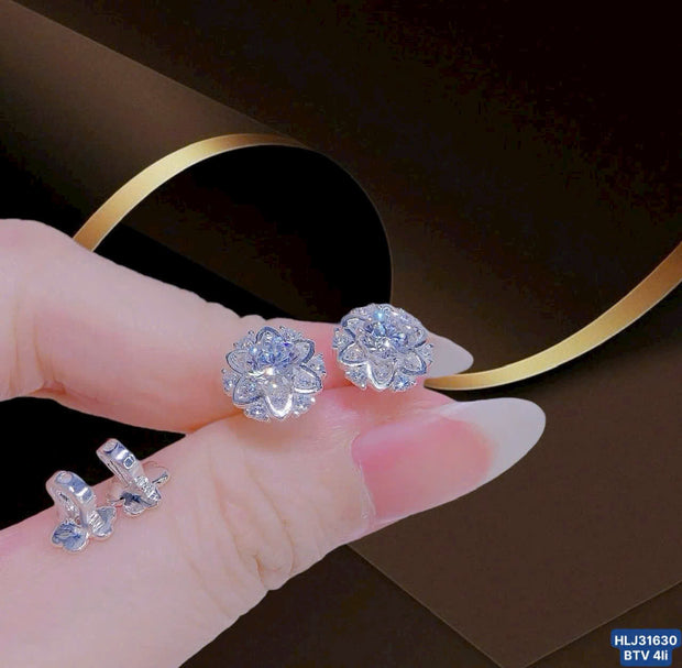 Silver flower-shaped earrings held by a hand with a dark background