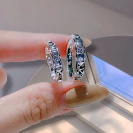 Silver hoop earrings being held by a hand with a neutral background
