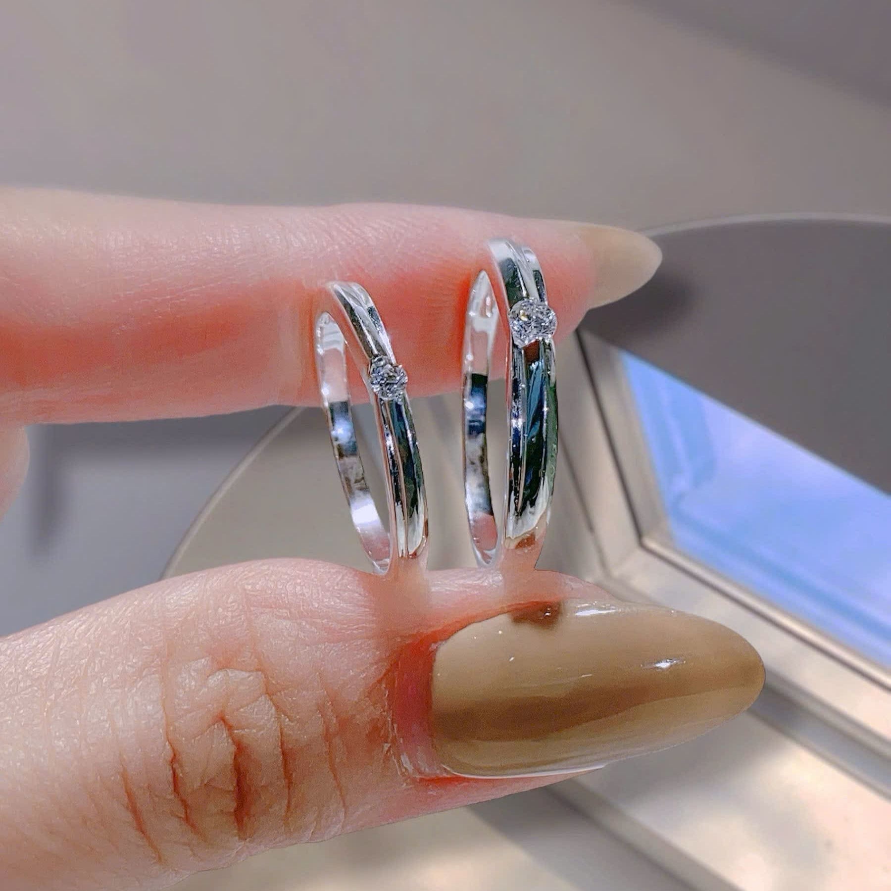 Silver hoop earrings being worn on a finger with a neutral background