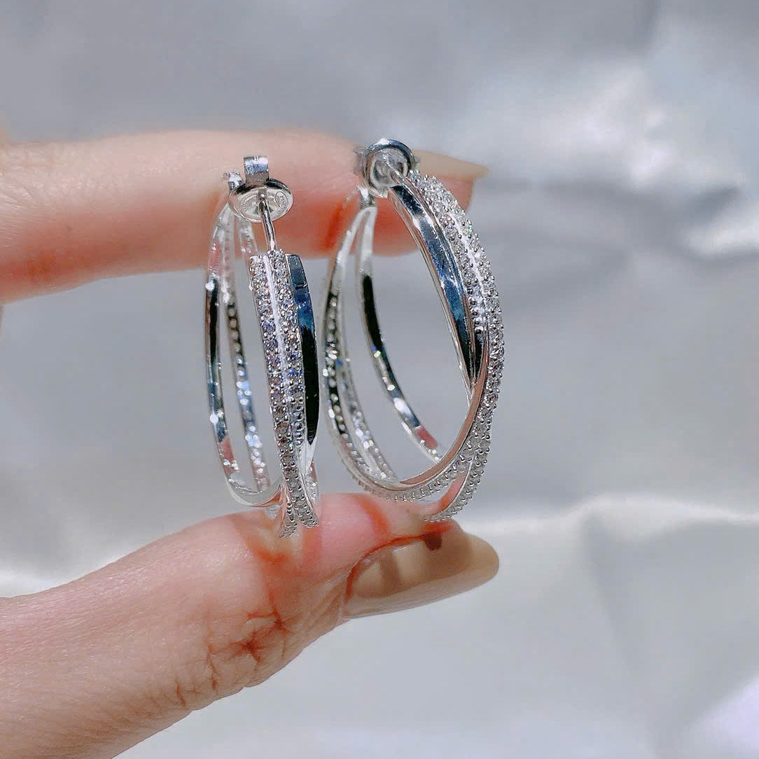 Silver hoop earrings held between fingers against a neutral background