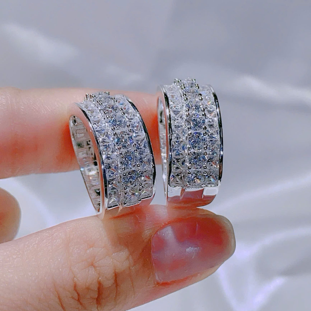 Silver hoop earrings held between fingers against a neutral background