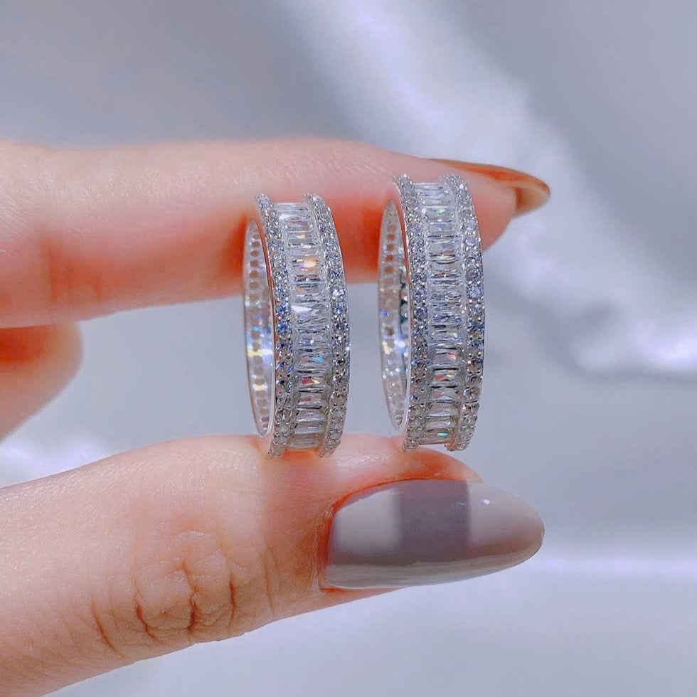 Silver hoop earrings held between fingers against a neutral background