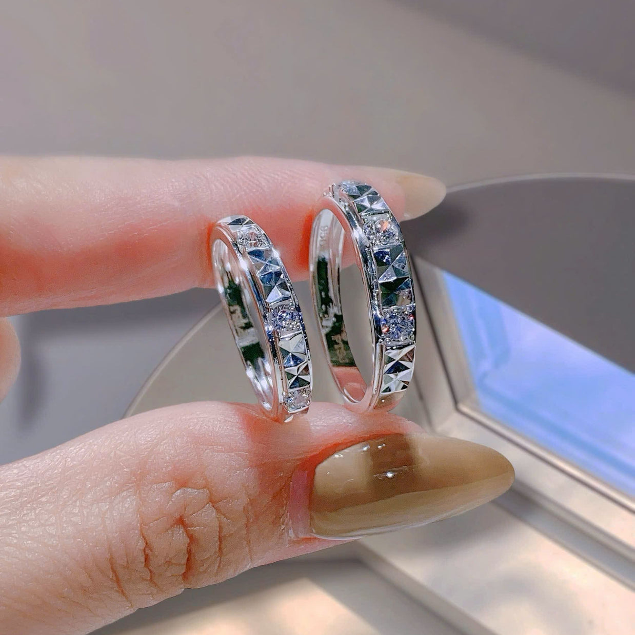 Silver hoop earrings held between fingers with a neutral background