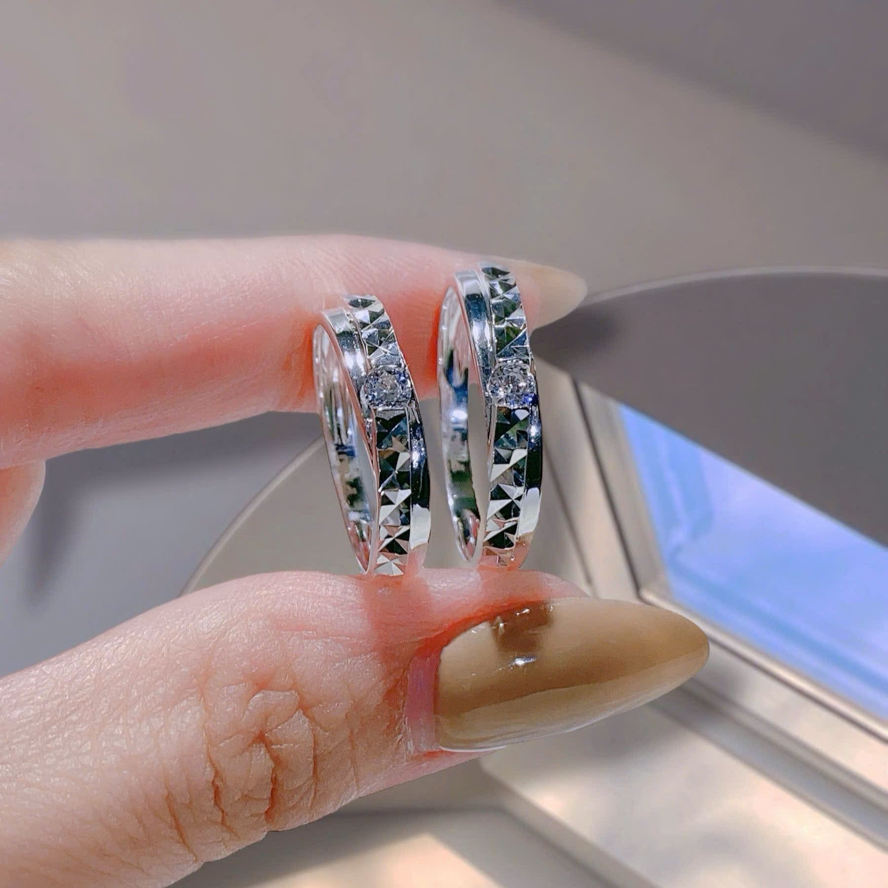 Silver hoop earrings held between two fingers against a neutral background