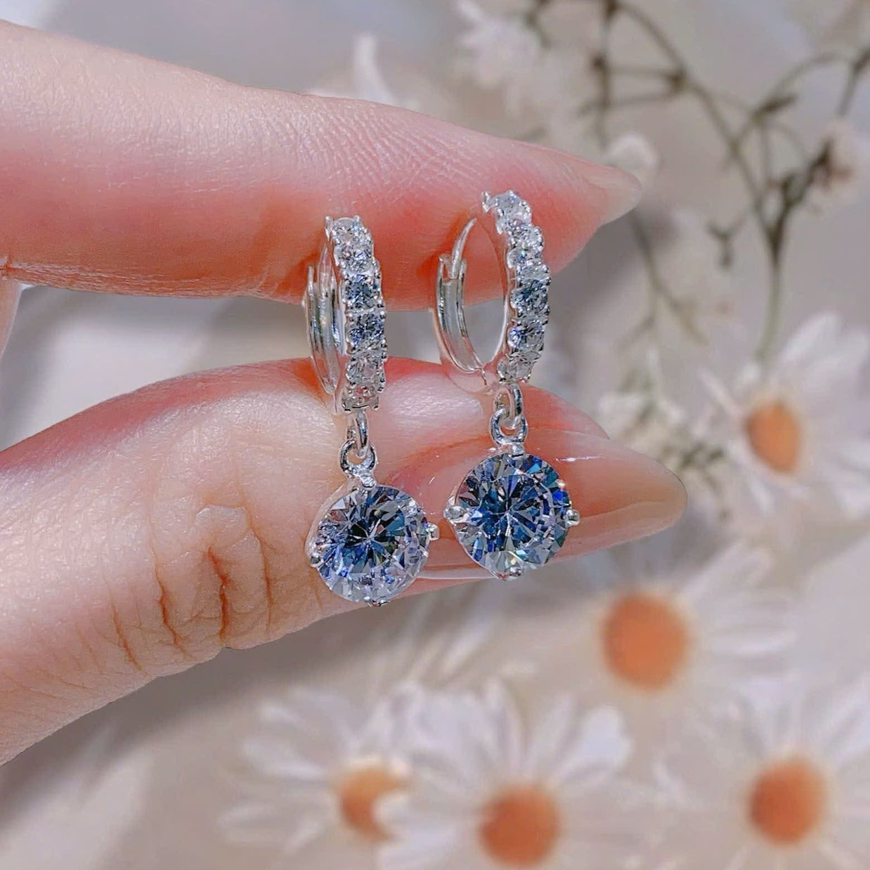 Silver hoop earrings with blue gemstones held between fingers against a floral background