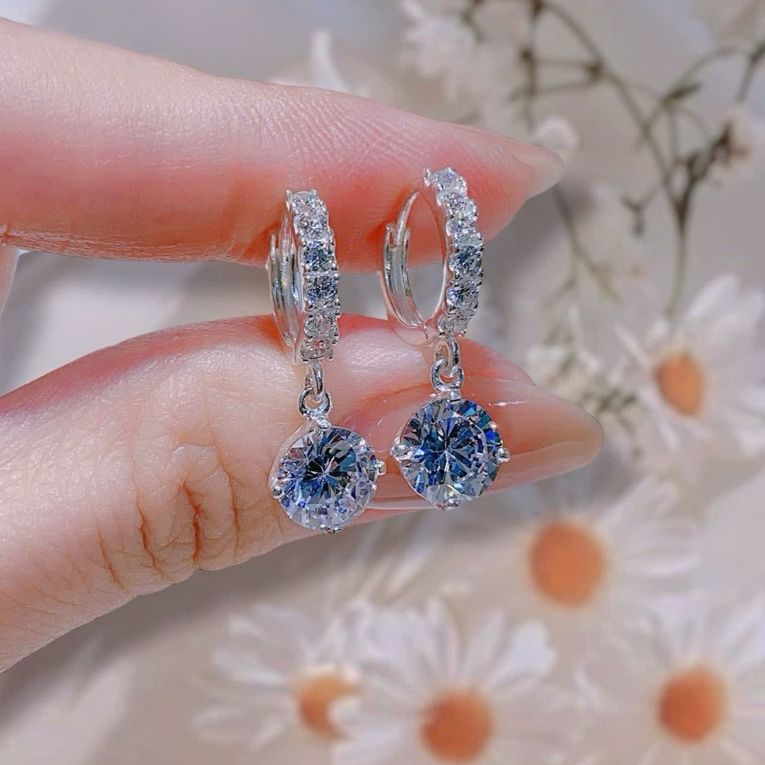 Silver hoop earrings with blue gemstones held between fingers against a floral background