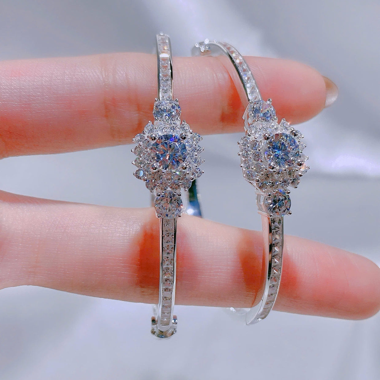 Silver hoop earrings with gemstones held between fingers against a blurred background