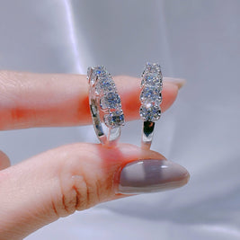 Silver hoop earrings with gemstones held between fingers against a neutral background