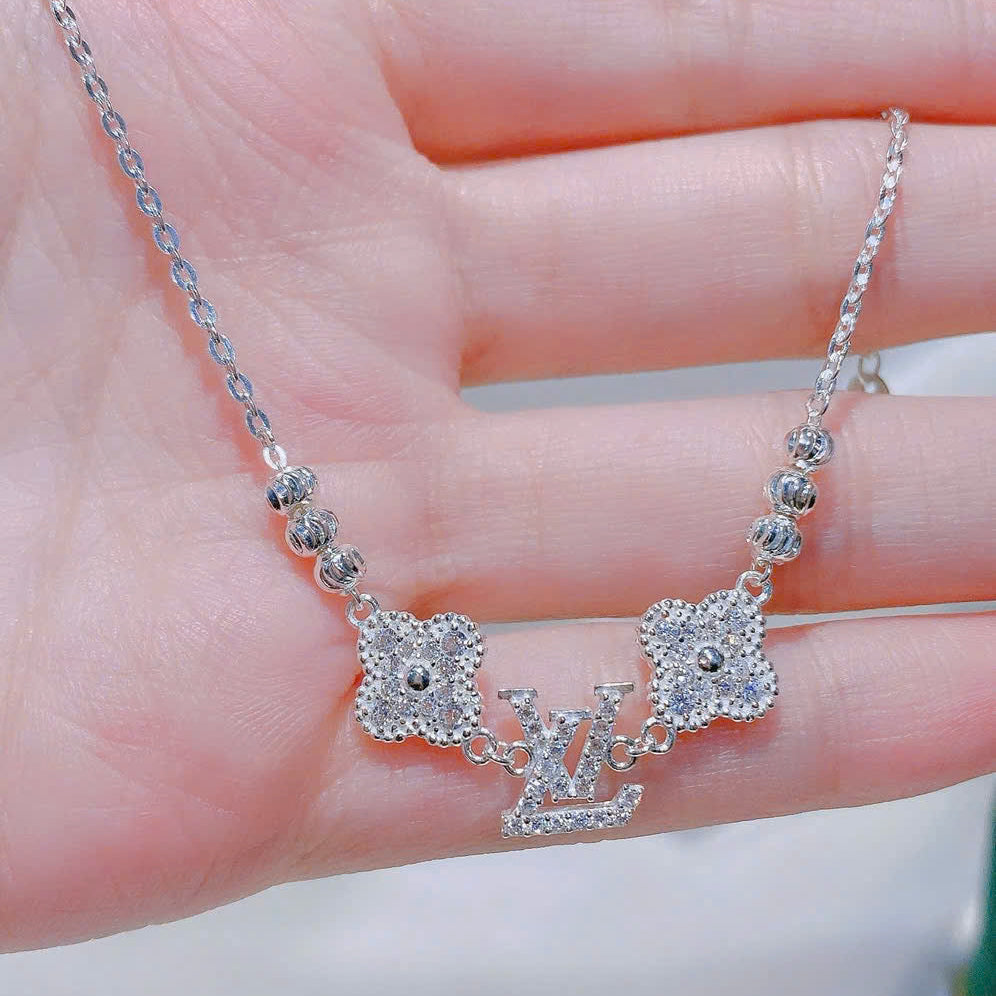 Silver necklace with 'LV' pendant held in a hand against a blurred background