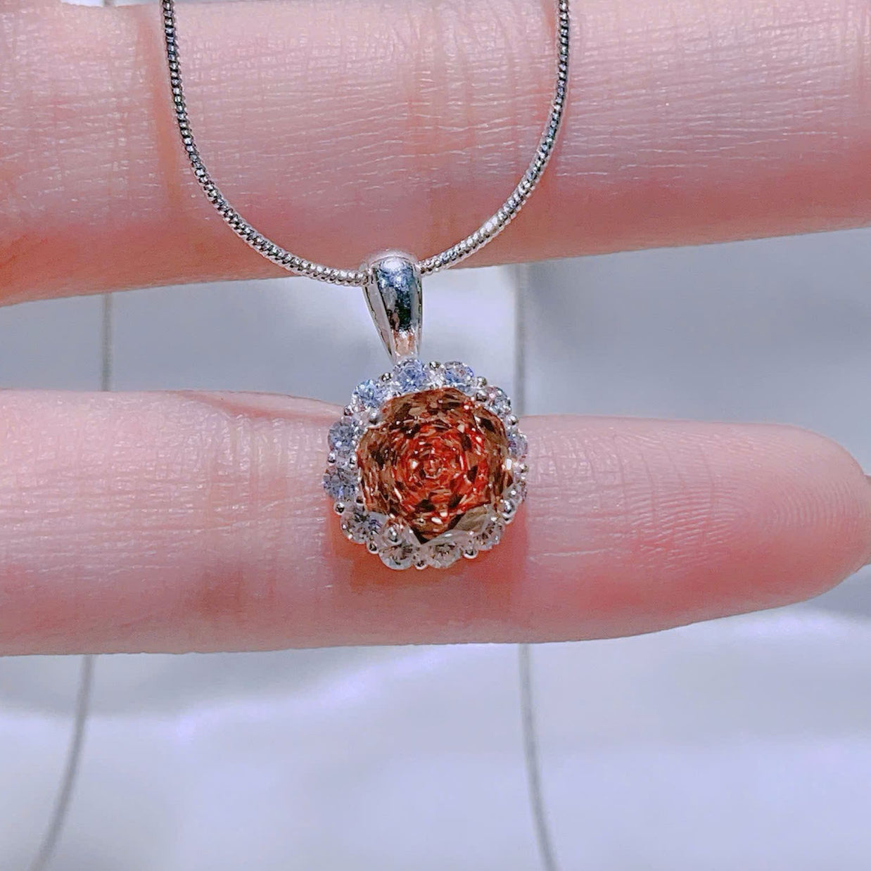 Silver necklace with a brown pendant held by a hand against a white background