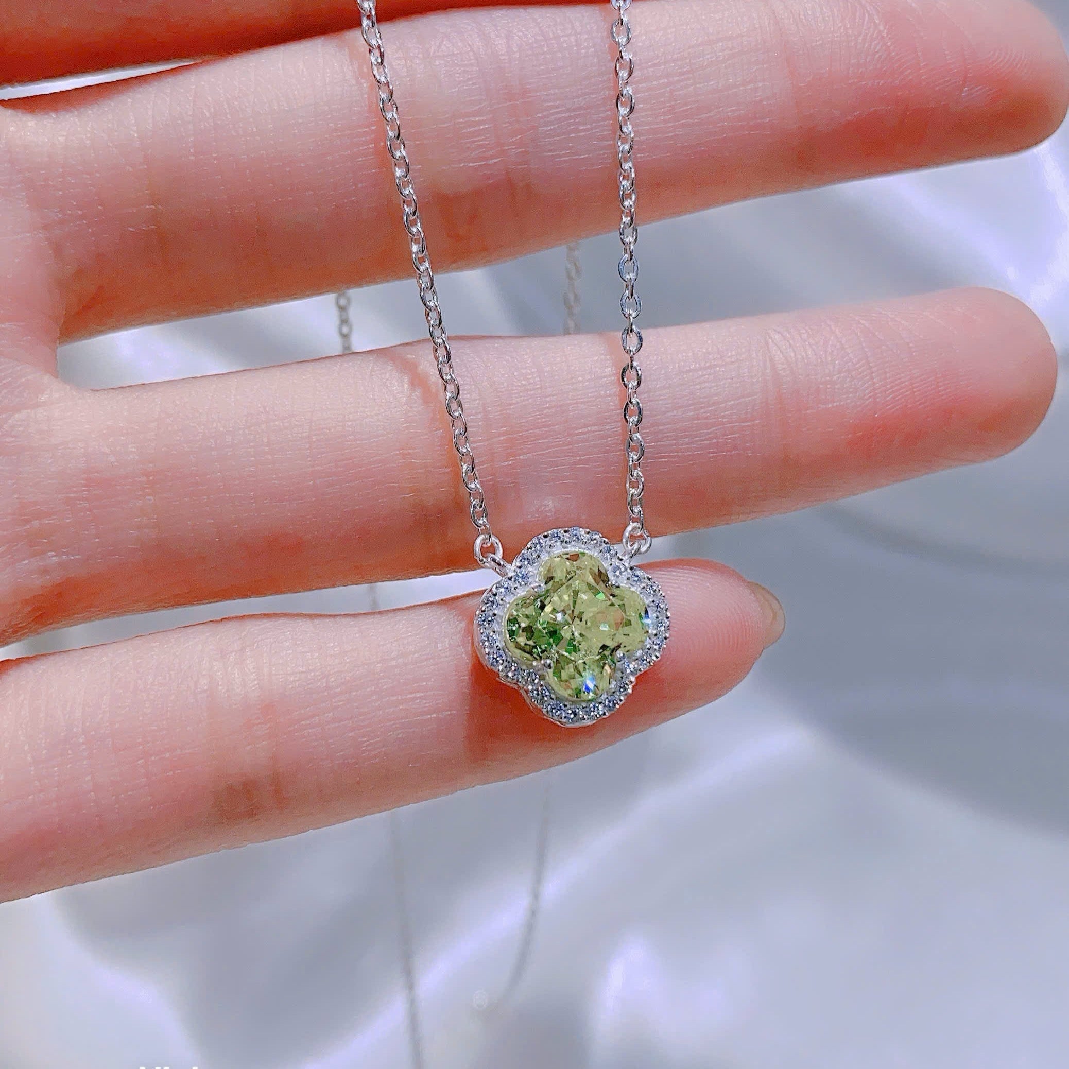 Silver necklace with a green gemstone pendant held by a hand against a white background