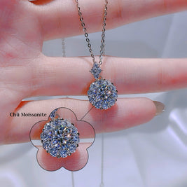 Silver necklace with a large pendant held between fingers against a neutral background