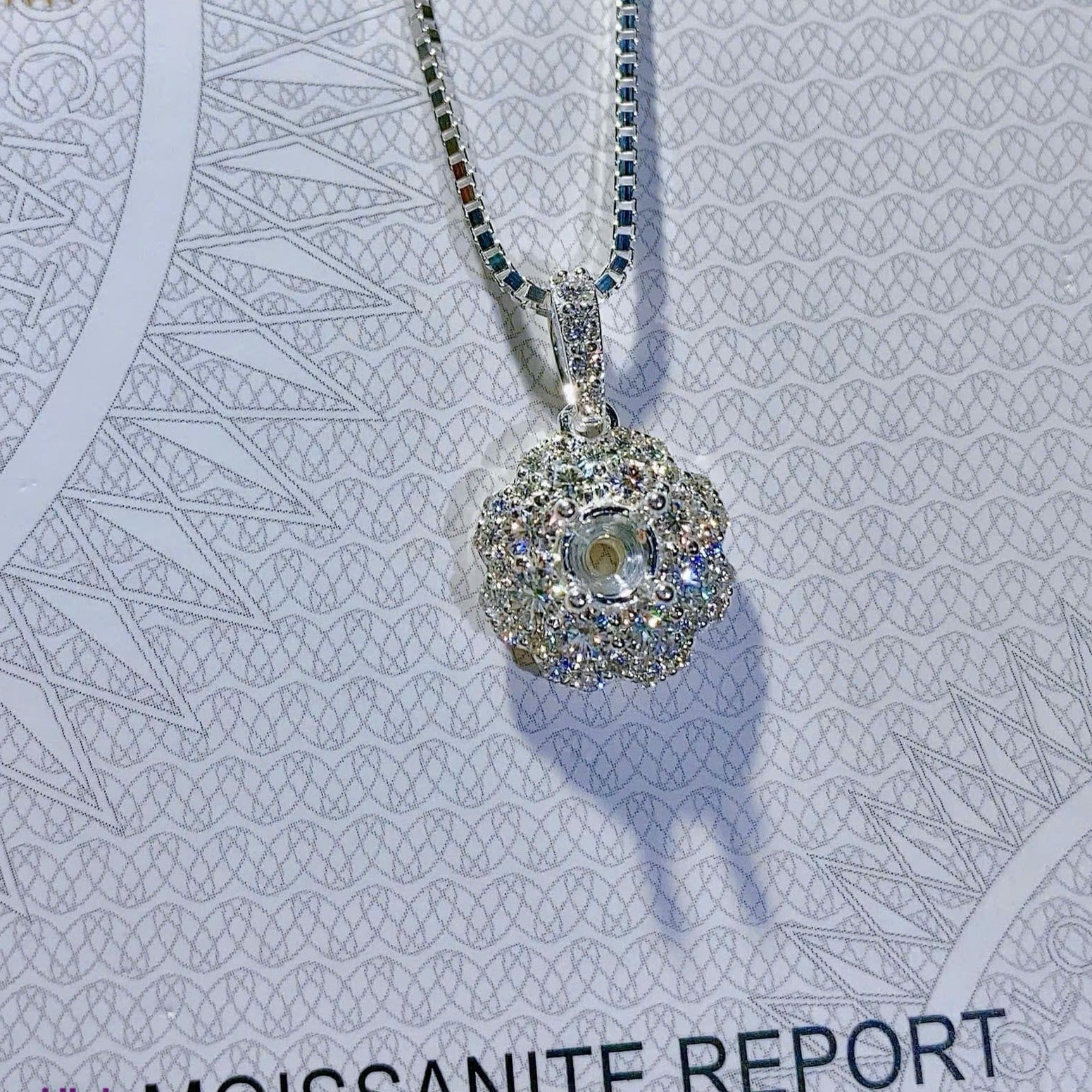 Silver necklace with a moissanite pendant on a GRA Moissanite Report card.