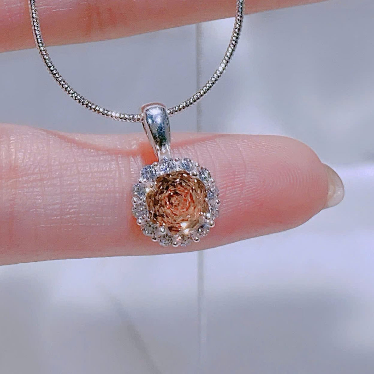 Silver necklace with a pendant on a hand against a blurred background