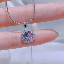 Silver necklace with a pink pendant held in a hand against a blurred background