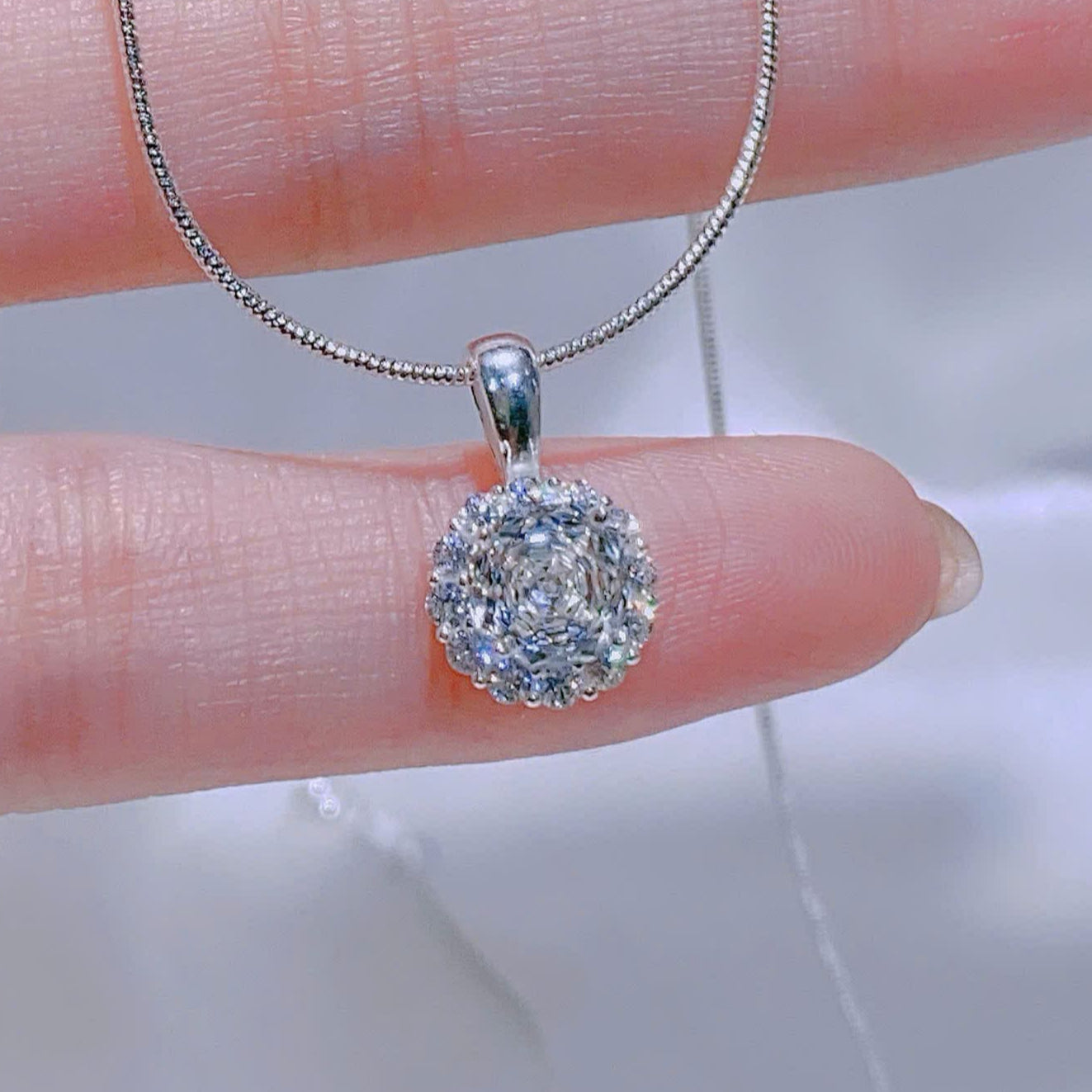Silver necklace with a round pendant held between fingers against a blurred background