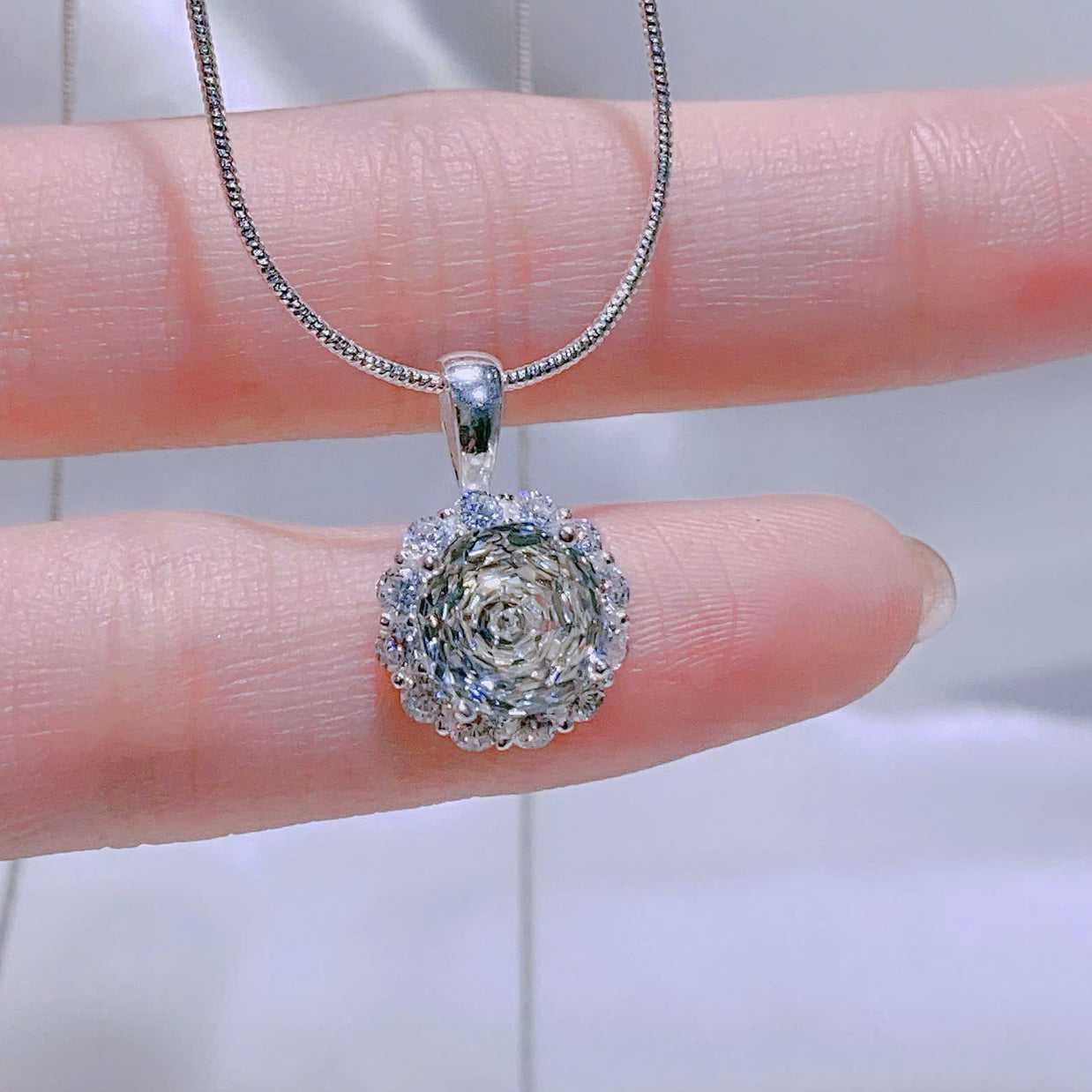 Silver necklace with a round pendant held by a hand against a neutral background
