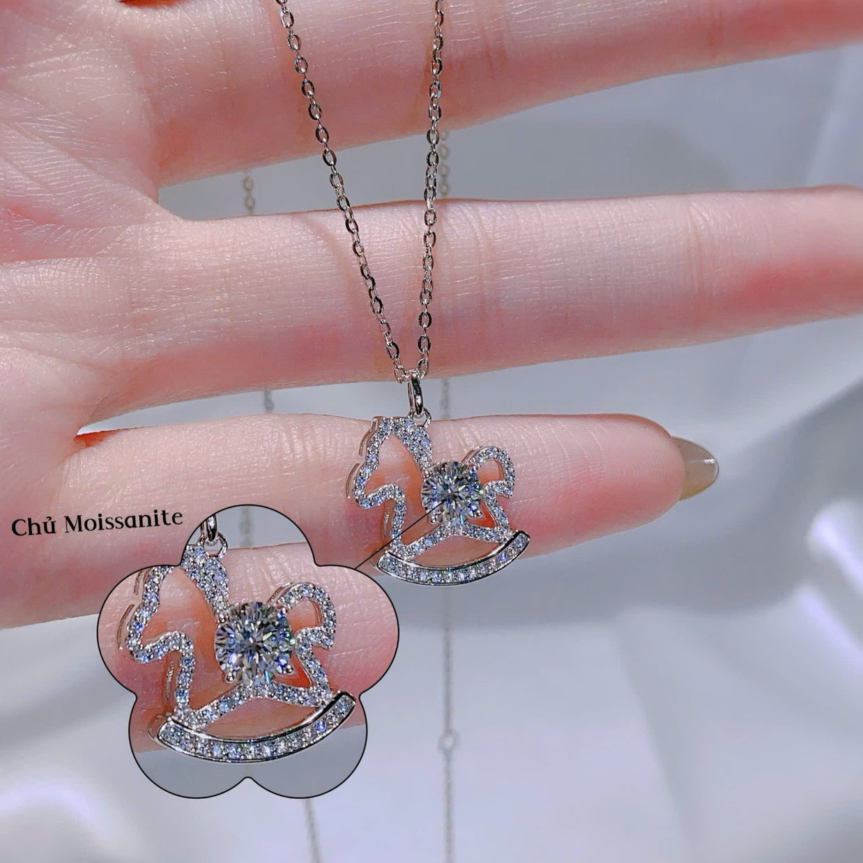 Silver necklace with pendant held by a hand against a neutral background