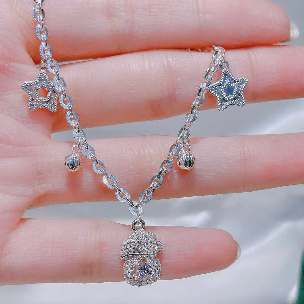 Silver necklace with star-shaped pendants on a hand against a neutral background