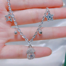 Silver necklace with star-shaped pendants on a hand against a neutral background