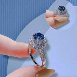 Silver ring with a blue gemstone held by a hand against a light blue background