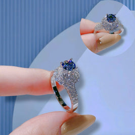 Silver ring with a blue gemstone held by a hand against a light blue background