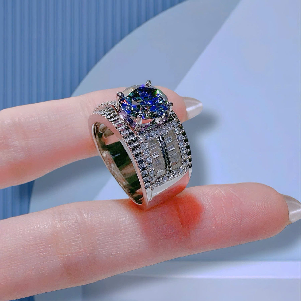 Silver ring with a blue gemstone on a finger against a light blue background