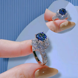 Silver ring with a blue gemstone on a finger against a light blue background