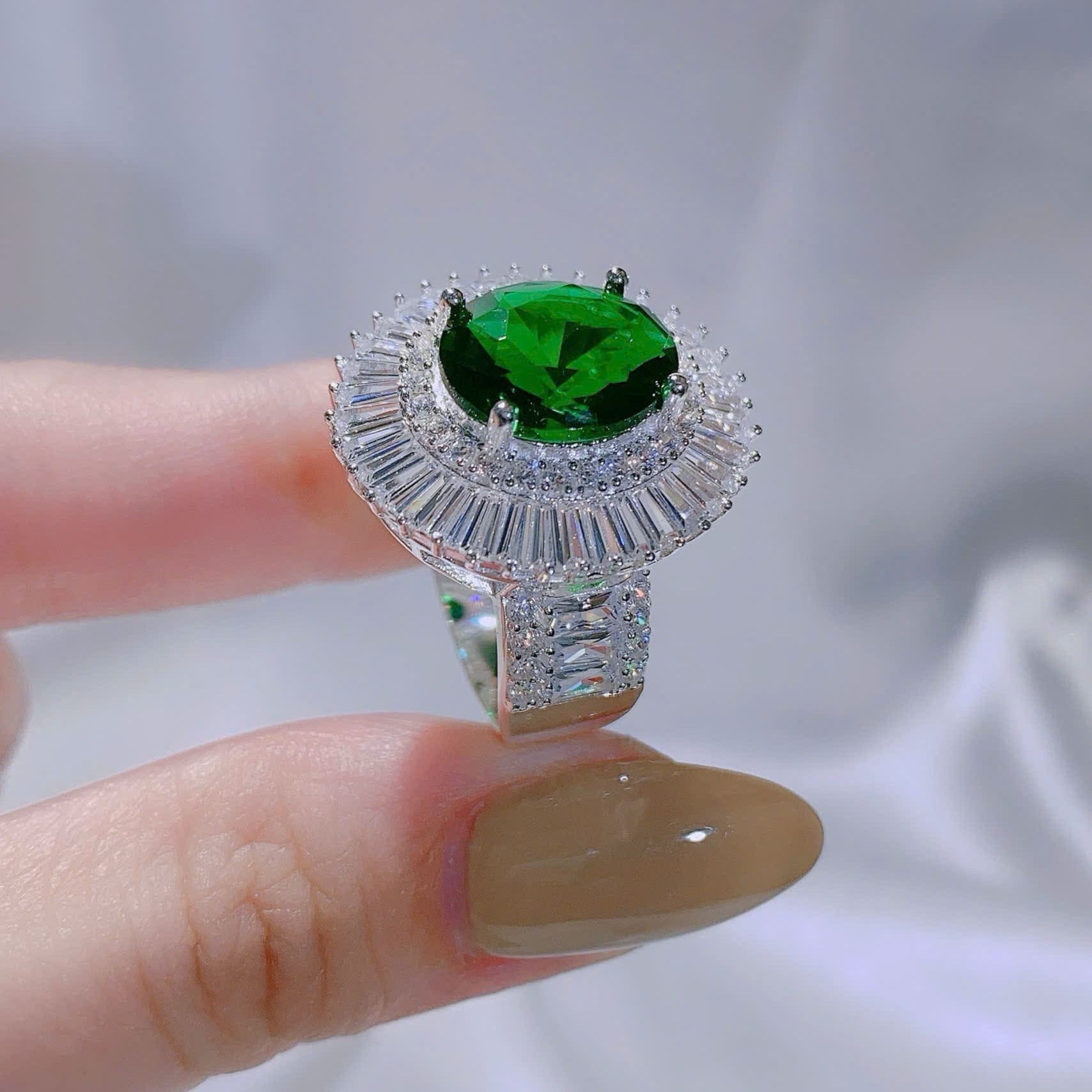 Silver ring with a green gemstone held by a finger against a white background