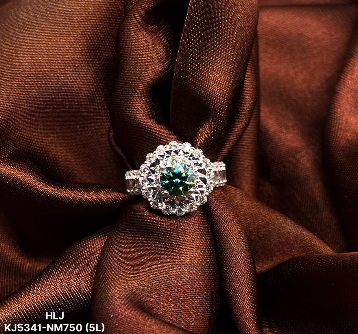 Silver ring with a green gemstone on brown fabric, brand 'HLJ' visible