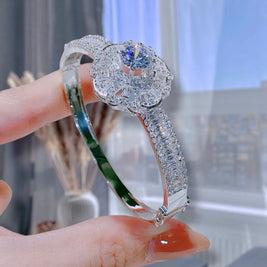 Silver ring with a large central gemstone held by a hand against a blurred indoor background