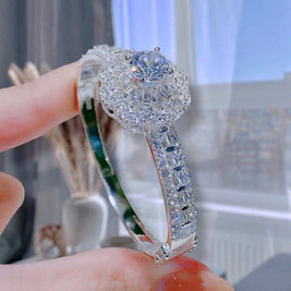 Silver ring with a large central gemstone held by a hand against a blurred indoor background
