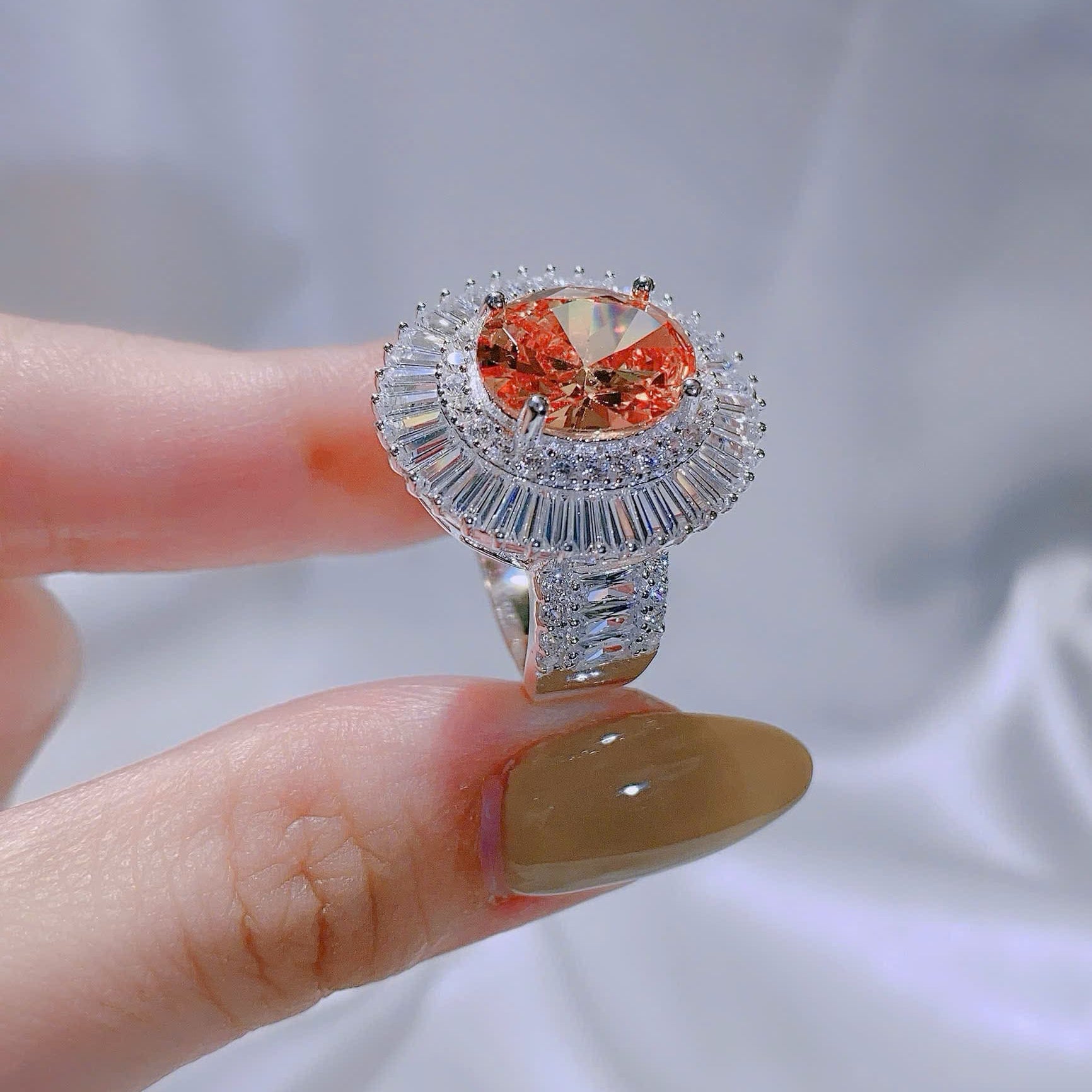 Silver ring with a large orange gemstone held by a hand against a light gray background