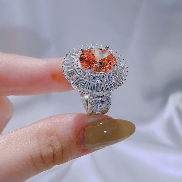 Silver ring with a large orange gemstone held by a hand against a light gray background