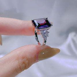Silver ring with a large purple gemstone held by a hand against a neutral background