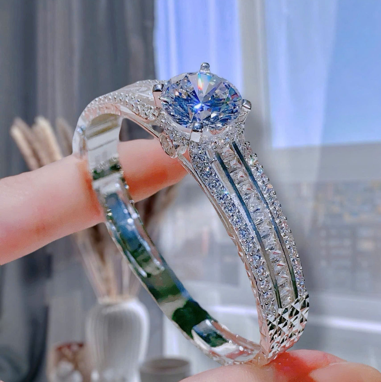 Silver ring with blue gemstone held by a hand against a blurred indoor background