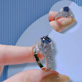 Silver ring with blue gemstone held by a hand against a light blue background