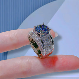 Silver ring with blue gemstone held on a finger against a light blue background