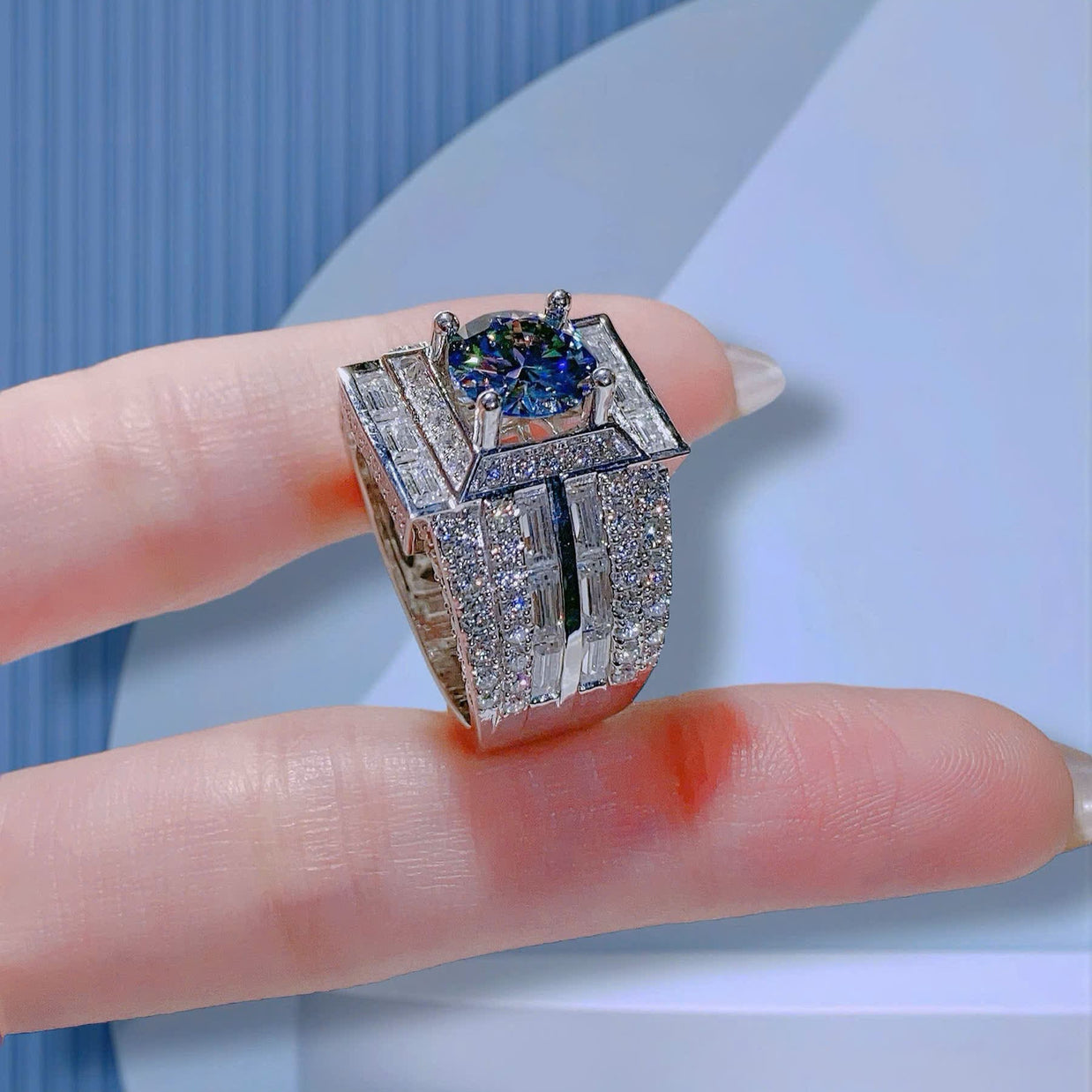 Silver ring with blue gemstone on a finger against a light blue background