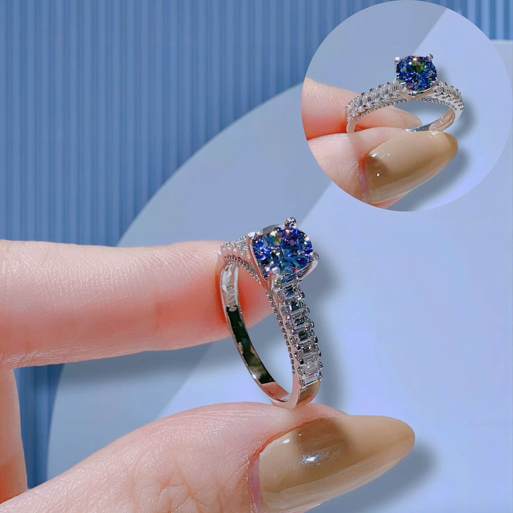 Silver ring with blue gemstones held by a hand against a light blue background