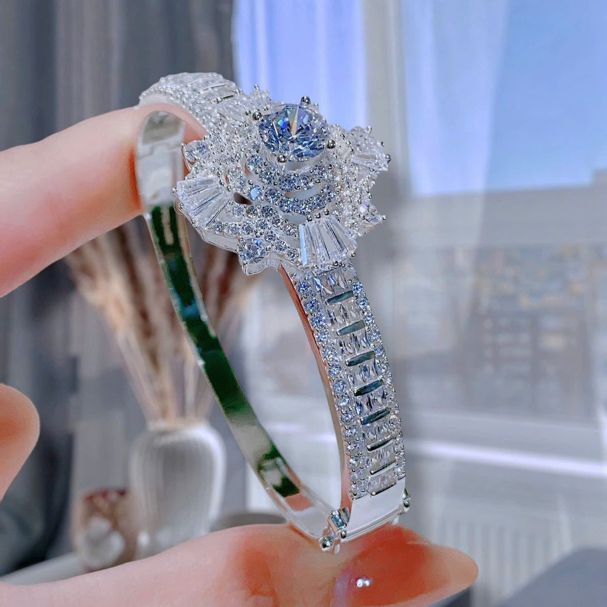Silver ring with floral design held by a hand against a blurred indoor background