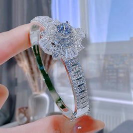 Silver ring with floral design held by a hand against a blurred indoor background
