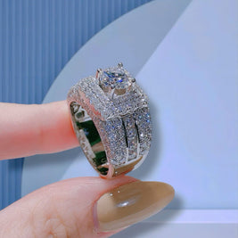 Silver ring with gemstone held by a hand against a light blue background