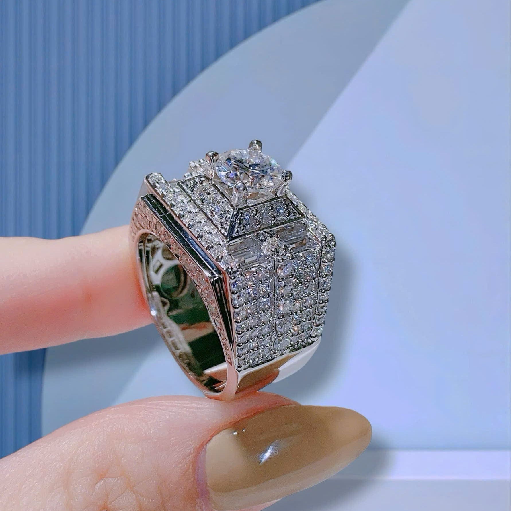 Silver ring with gemstones held by a hand against a light blue background